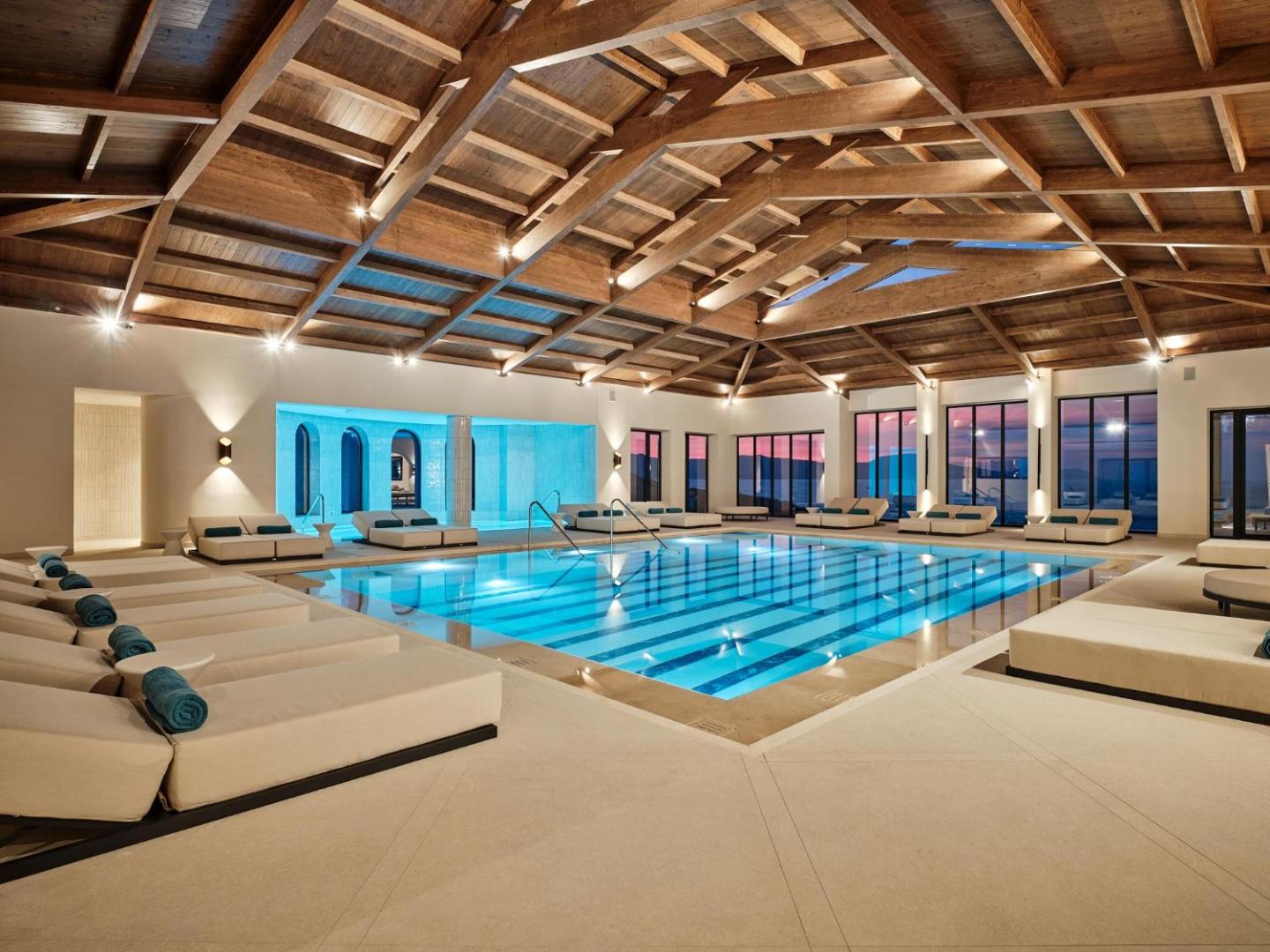 Plašs iekštelpu baseins ar atpūtas gultām zem masīvām koka griestu konstrukcijām.