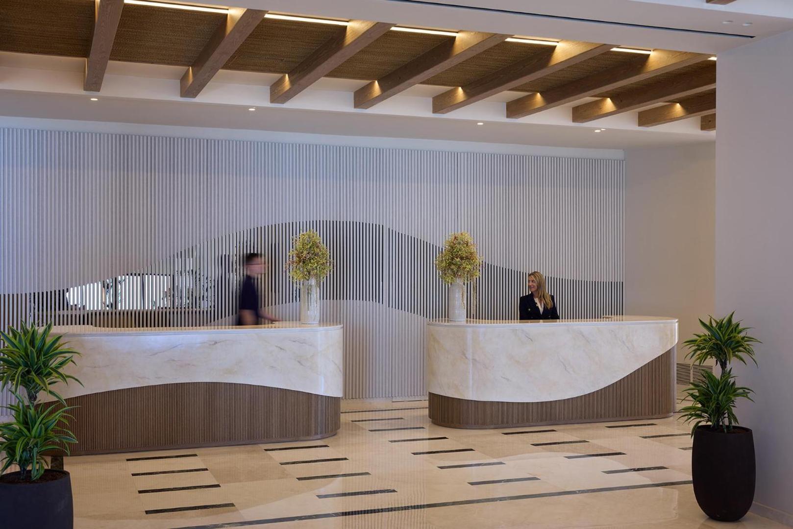 Viesnīcas recepcijas zona ar gaišām marmora letēm un modernu koka siju griestu dizainu.