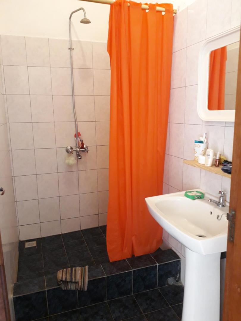 Viesnīcas vannas istaba ar dušu, oranžu aizkaru, izlietni un spoguli.