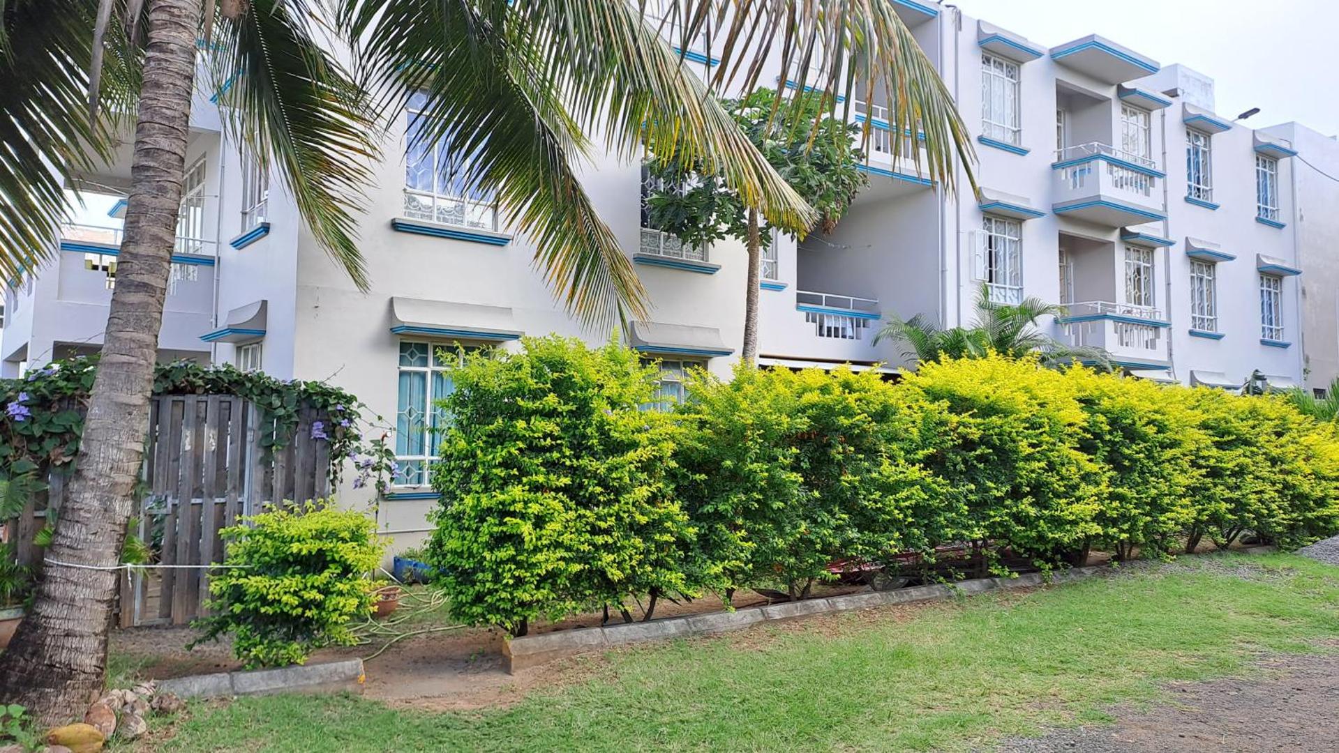 Viesnīcas Allamanda ēkas fasāde ar balkoniem, ko ieskauj palmas un zaļi krūmi.