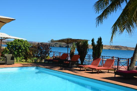 Āra baseins ar sarkaniem sauļošanās krēsliem piekrastē zem zilām debesīm.