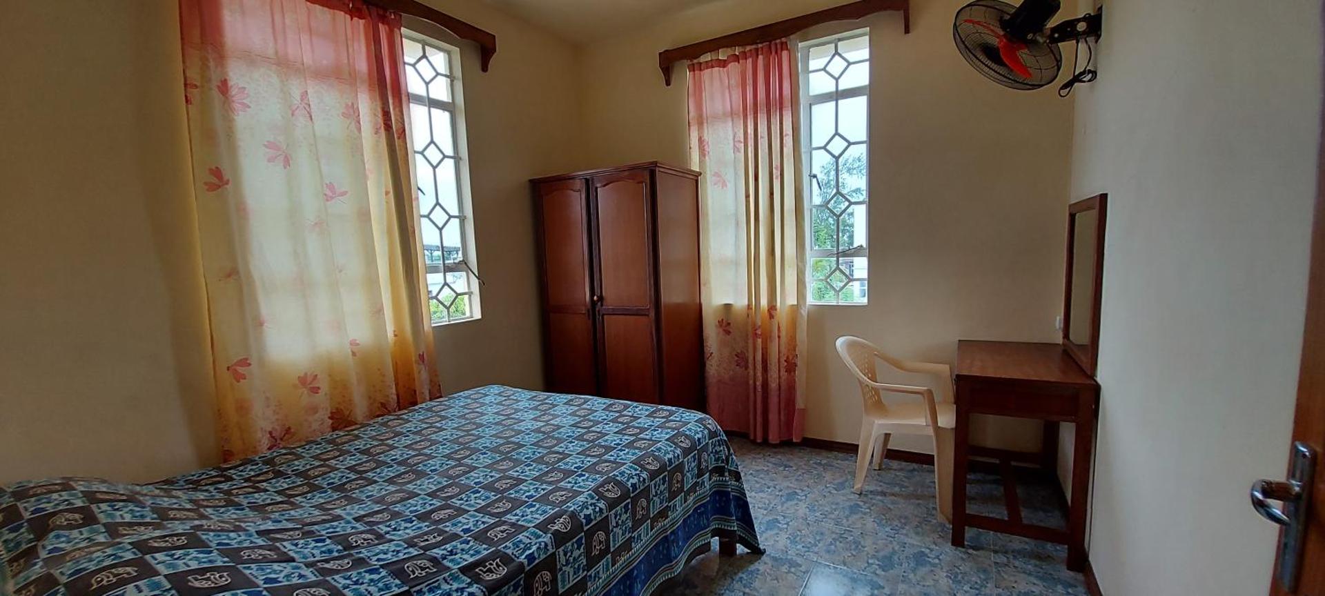 Viesnīcas numurs ar divguļamo gultu, koka skapi un darba galdu pie loga.