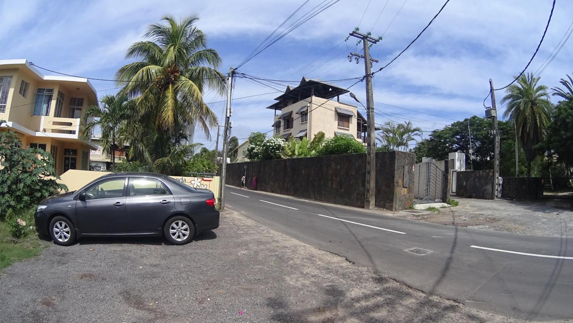 Skats uz ielu un viesnīcas Allamanda apkārtni ar automašīnu priekšplānā.