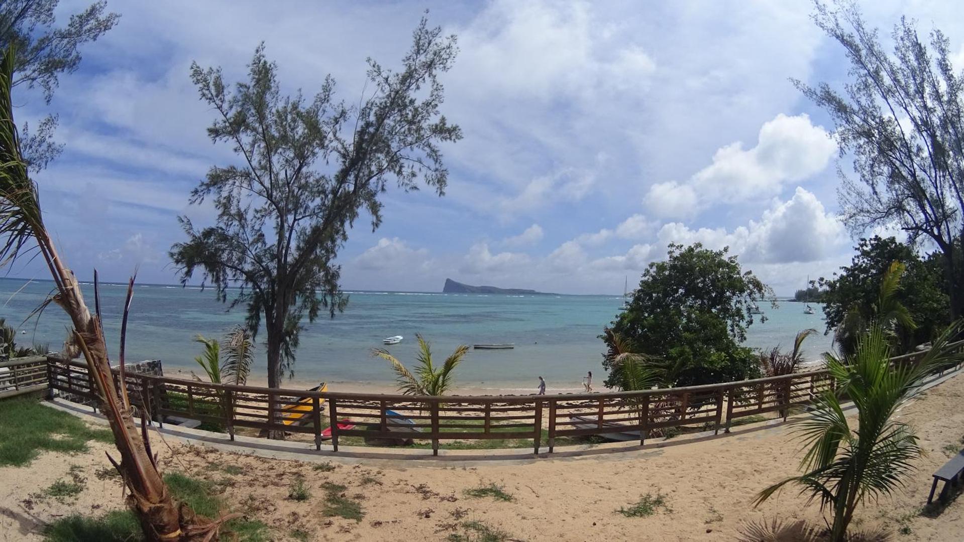 Panorāmas skats uz piekrasti, koka nožogojumu un tālām laivām okeānā.