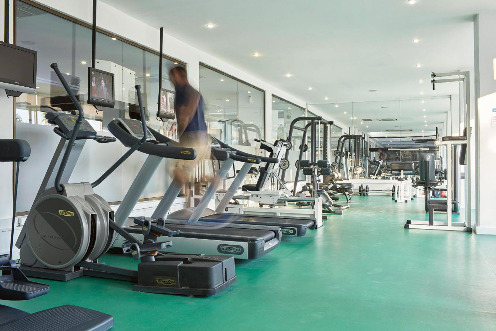 Grecian Bay fitness centrs ar moderniem Technogym skrejceļiem un trenažieriem gaišā telpā ar spoguļiem