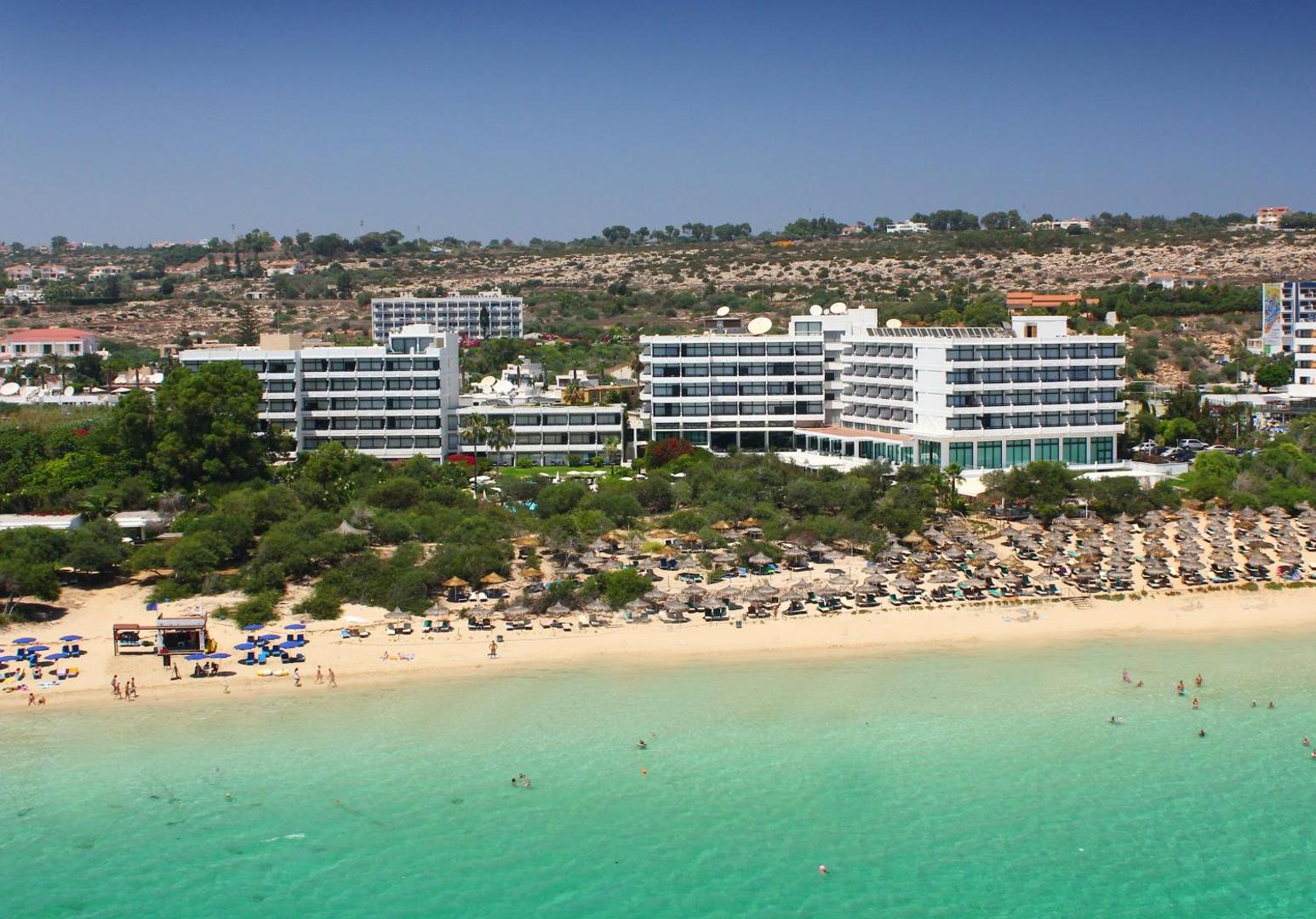 Grecian Bay viesnīcas panorāmas skats no putna lidojuma Aijanapā, Kiprā — balta smilšu pludmale, tirkīza ūdens un kūrorta ēkas