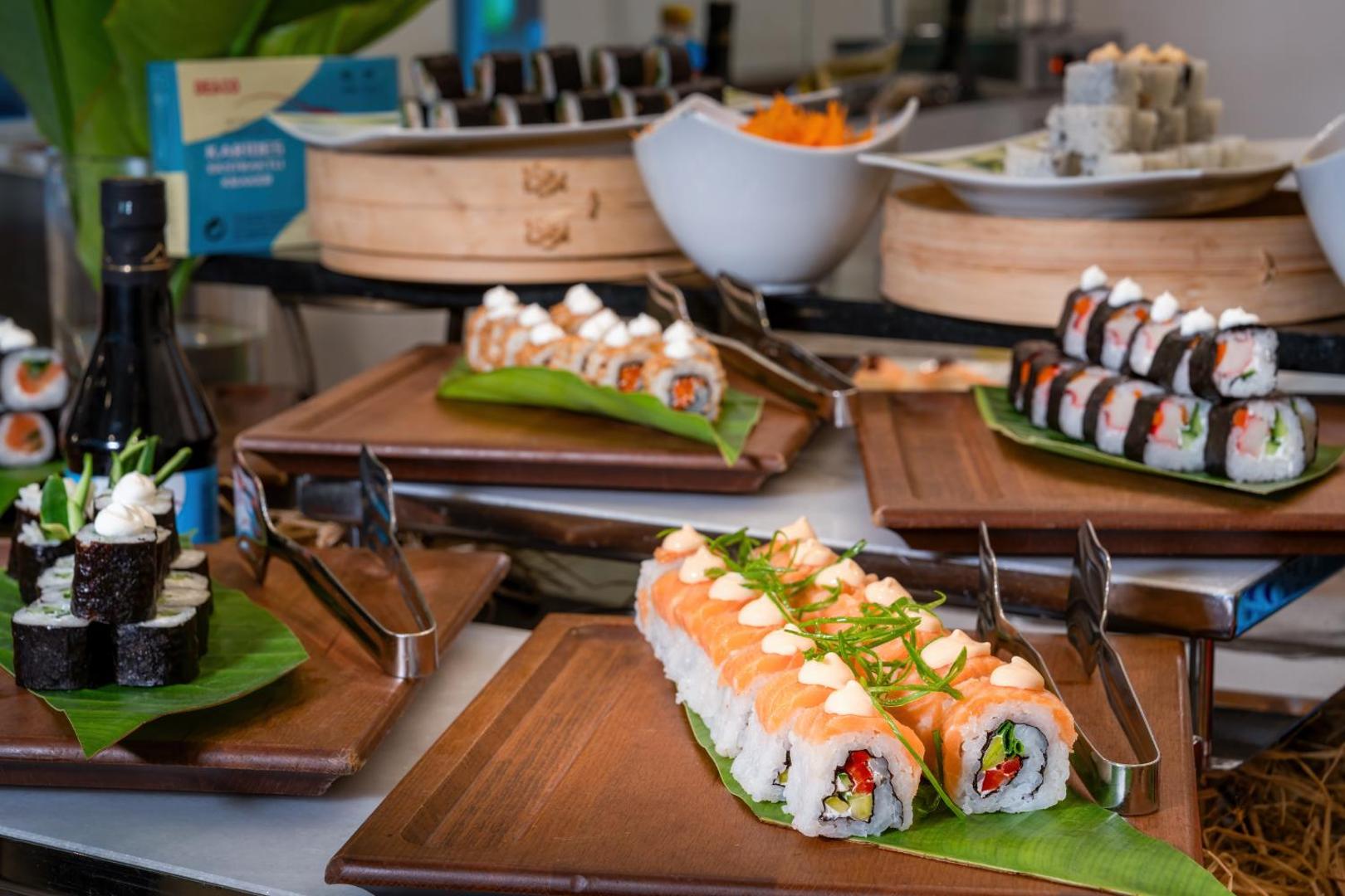 Dažādu suši veidu izlase uz koka dēlīšiem viesnīcas restorāna bufetē.