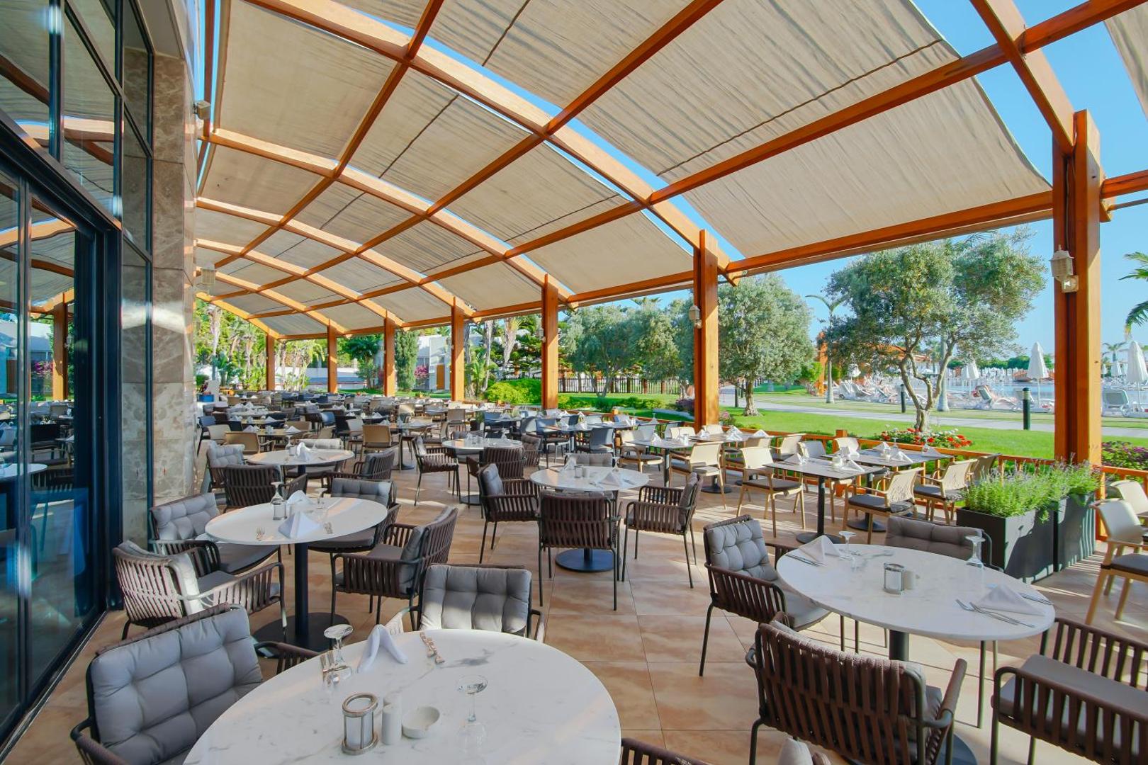 Viesnīcas Baia Lara āra terases restorāns ar daudziem galdiņiem zem saulessarga nojumes.