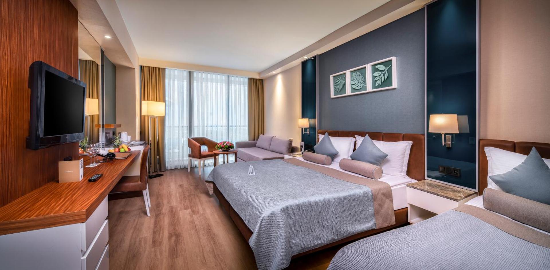 Plašs viesnīcas numurs ar divguļamo gultu, papildu gultu un dīvānu atpūtas zonā.