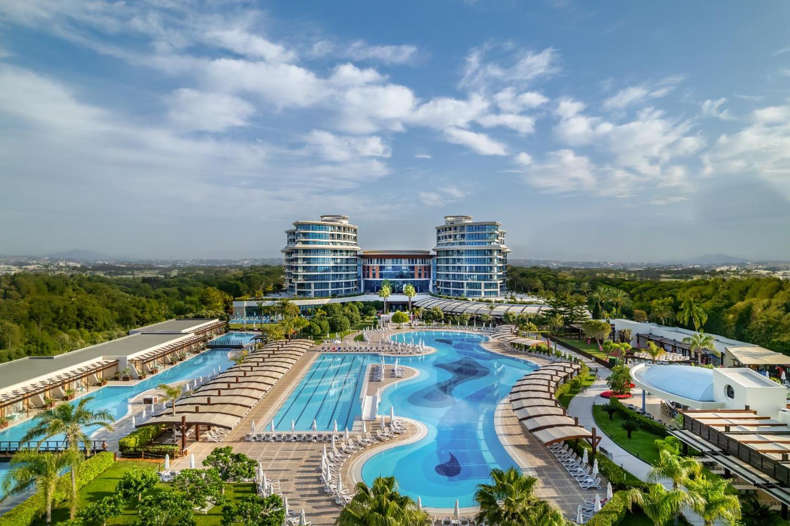 Viesnīcas Baia Lara galvenā ēka un plašais peldbaseinu komplekss saulainā dienā.