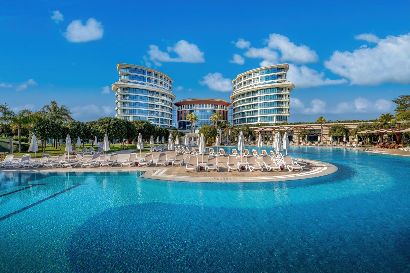 Baia Lara viesnīcas ēkas un liels, zils baseins ar sauļošanās krēsliem priekšplānā.