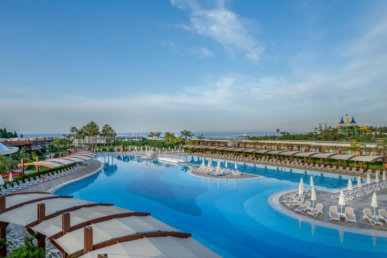 Plašs baseins ar daudziem sauļošanās krēsliem un skatu uz jūru tālumā.