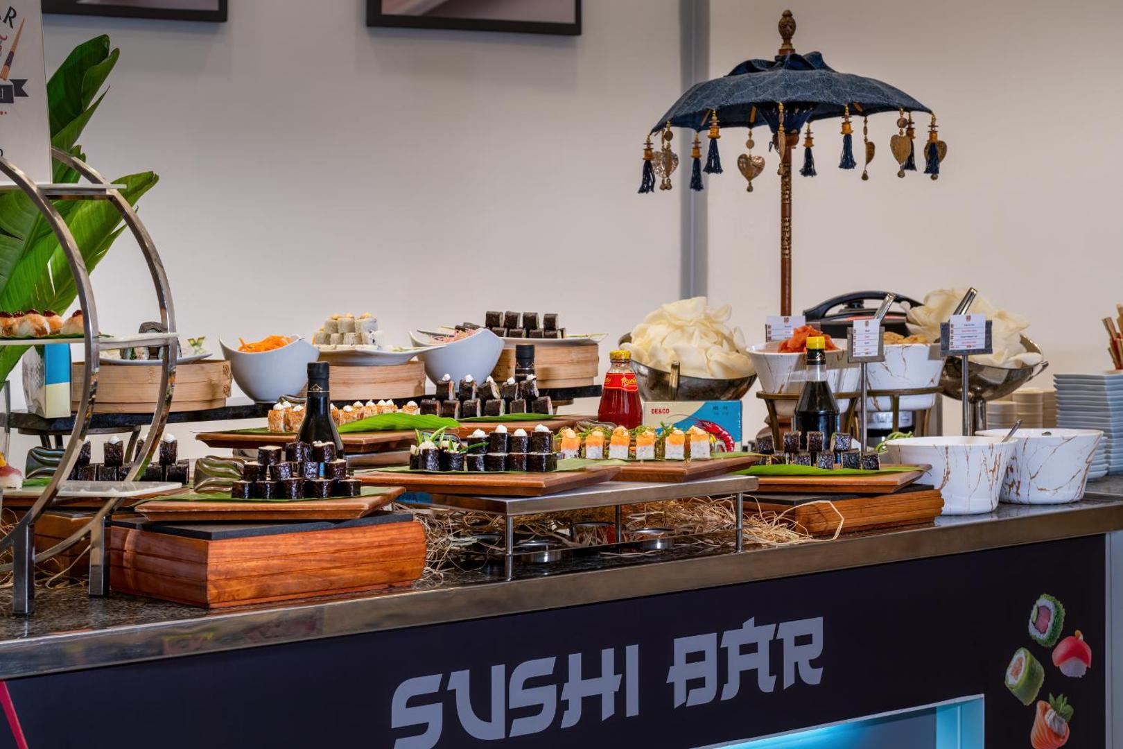 Viesnīcas Baia Lara suši bāra lete ar dekoratīvu saulessargu un uzkodu klāstu.
