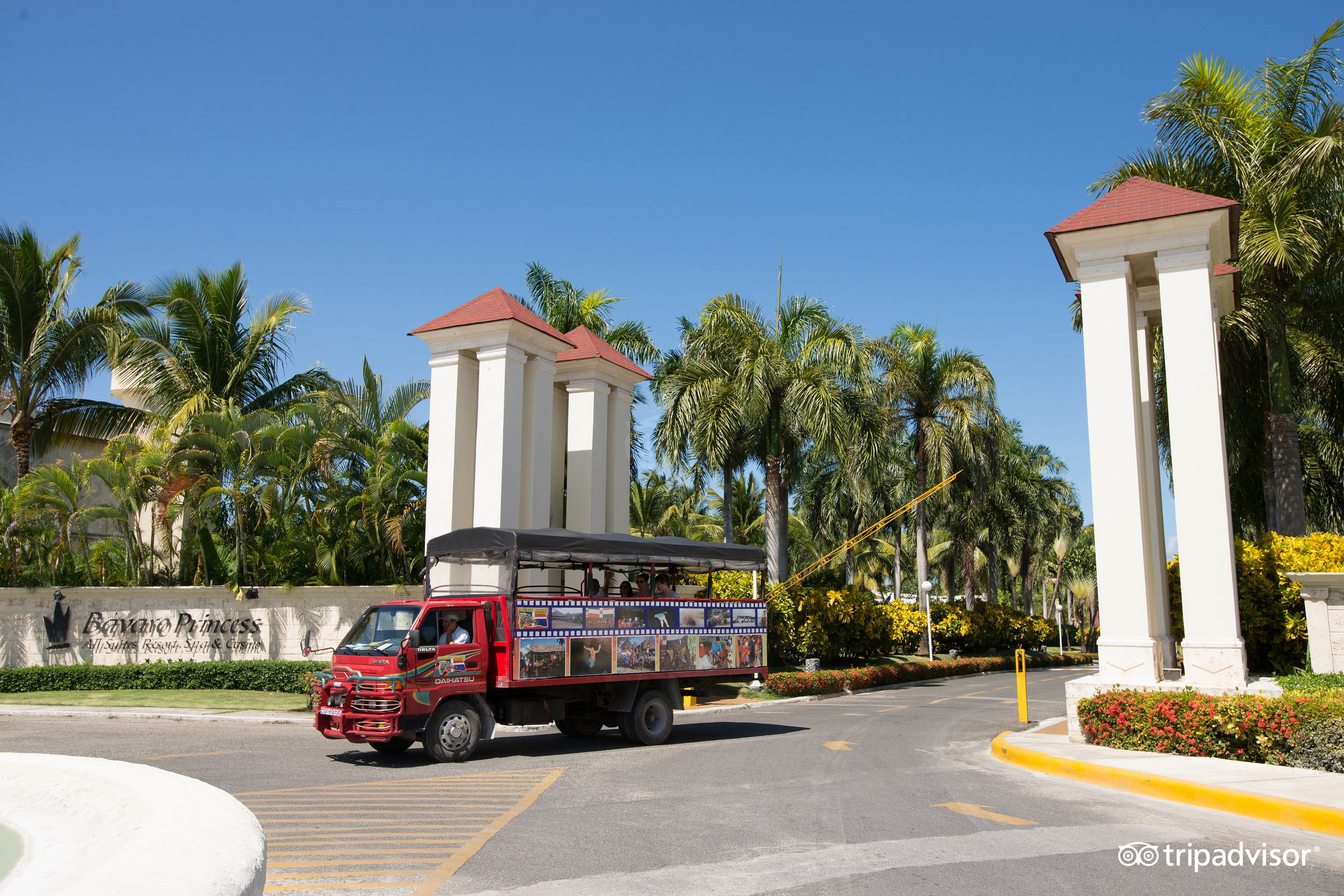 Grand Bavaro Princess galvenā ieeja ar viesnīcas nosaukumu uz sienas un sarkano tūristu transportu, kas pārvadā viesus