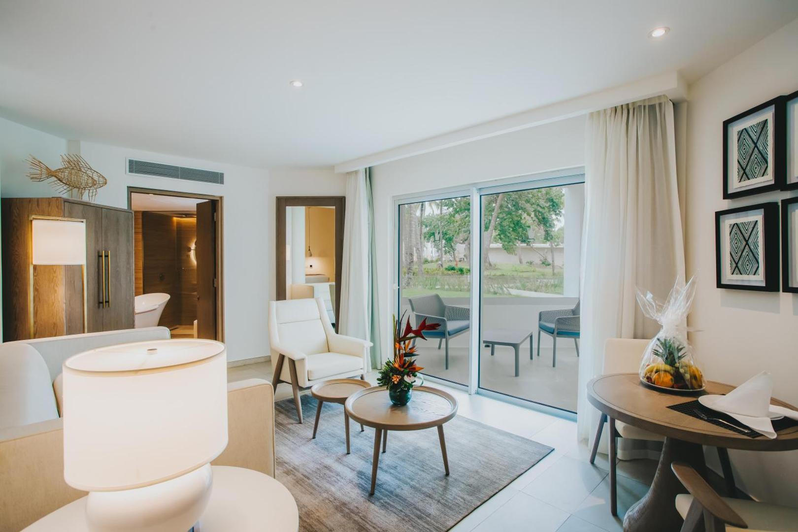 Viesnīcas numura interjers ar skatu caur lieliem stikla logiem uz dārzu.