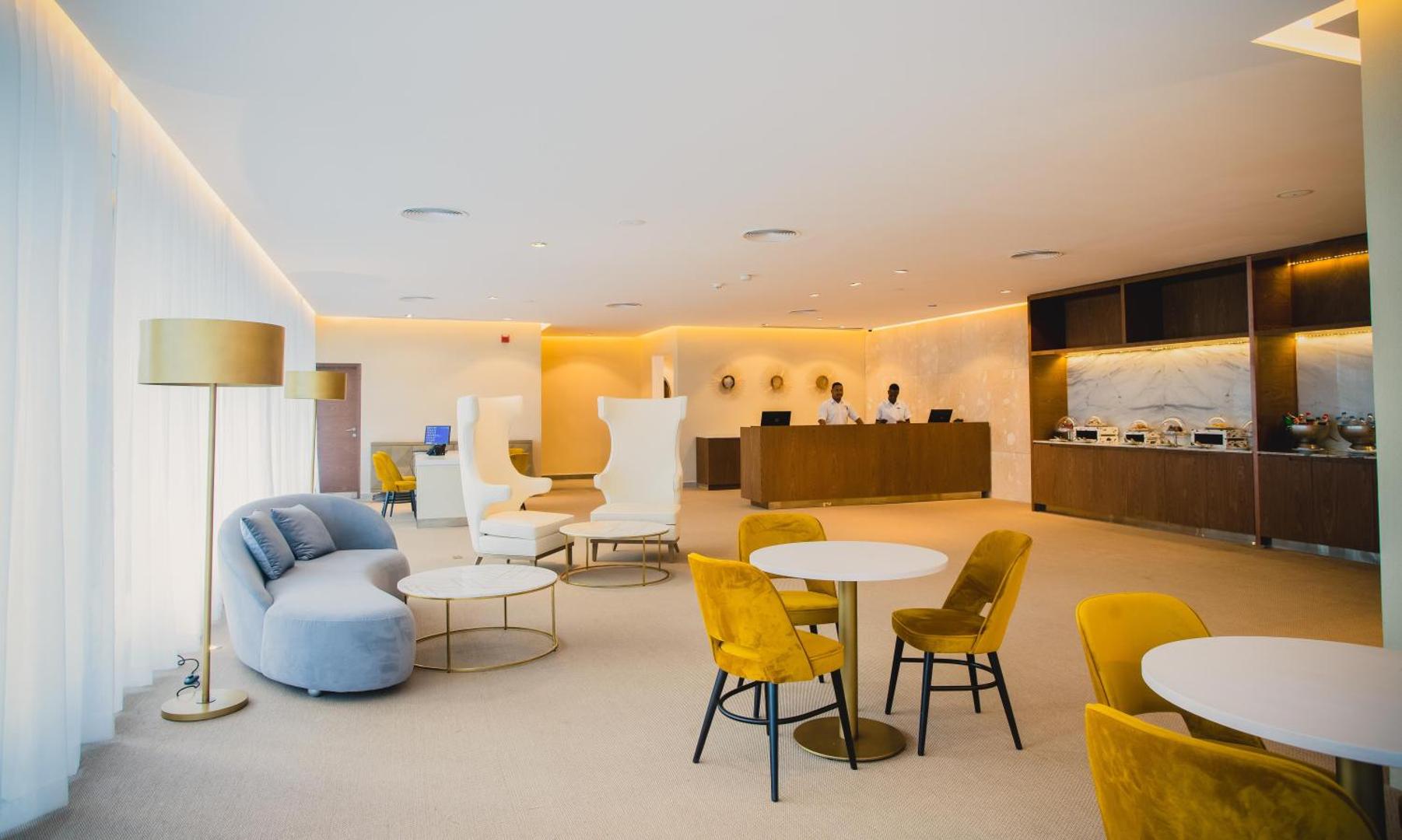 Gaiša atpūtas telpa ar dzelteniem krēsliem un zilu dīvānu Grand Bavaro Princess viesnīcā.
