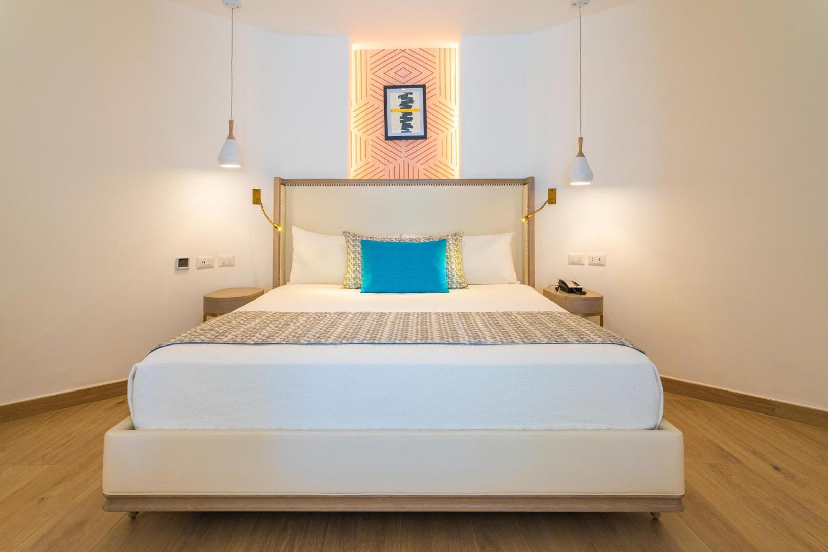 Mūsdienīgs viesnīcas numurs ar lielu divguļamo gultu un koši zilu dekoratīvo spilvenu.