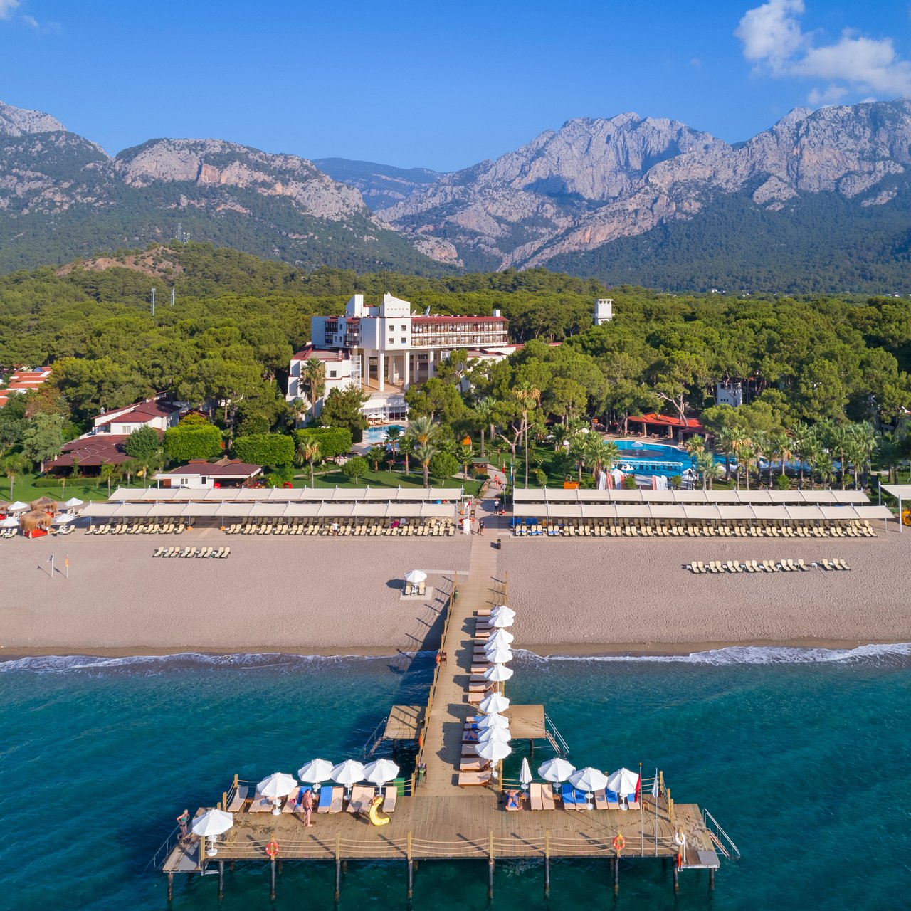 Seven Seas Hotel Life panorāmas skats no putna lidojuma Kemeras reģionā — viesnīcas ēka, plaša pludmale, koka piestātne un kalnu fons