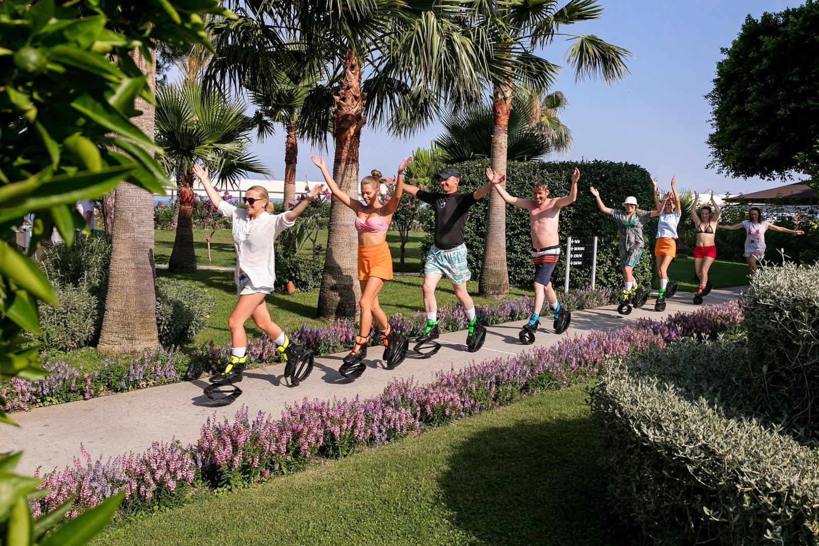 Viesnīcas Seven Seas Hotel Life viesi nodarbojas ar Kangoo Jumps fitnesu palmu dārzā uz gājēju celiņa