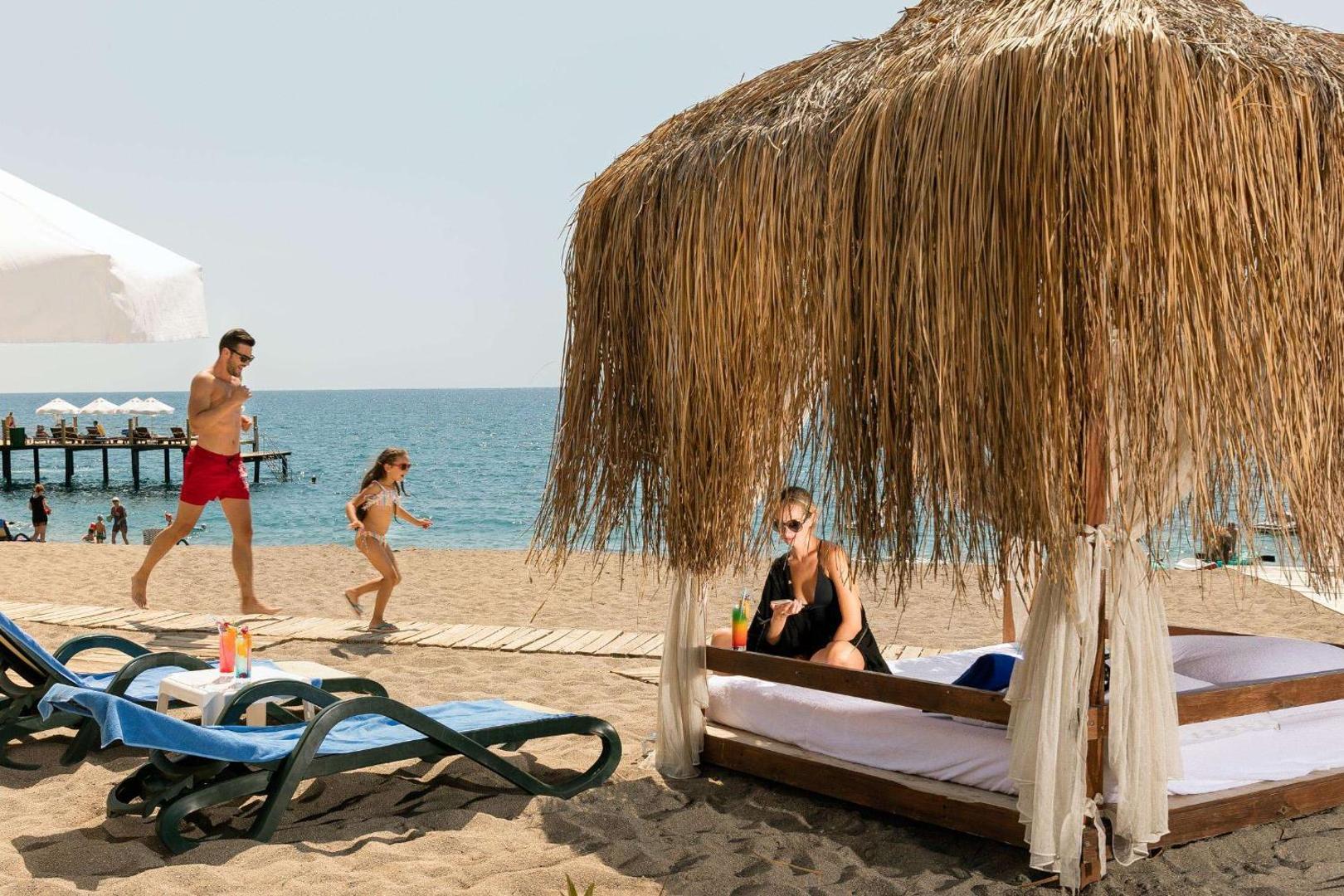 Seven Seas Hotel Life pludmales atpūtas zona ar privātu bungalo tipa nojumi, kurā atpūšas sieviete, un bērnu fonā