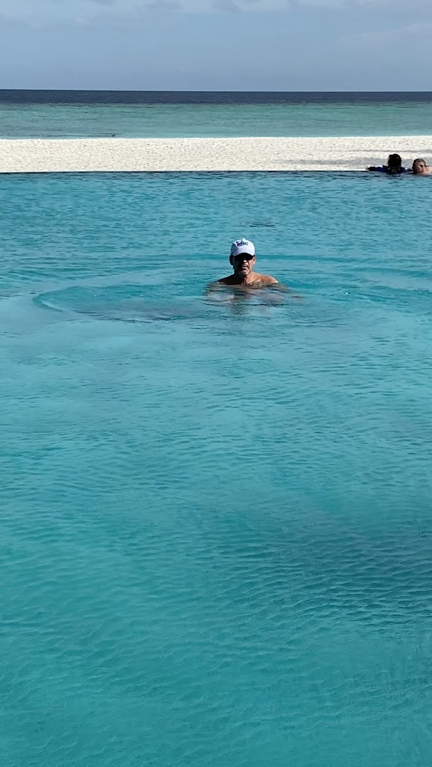 Viesis peldas Veligandu Maldives Resort Island dzidrajā okeāna ūdenī pie baltas smilšu sēkles saulainā dienā