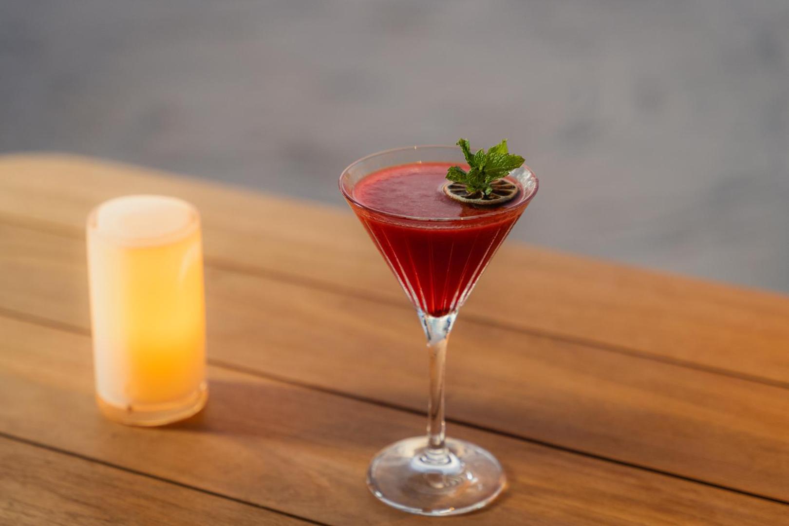 Elegants sarkans kokteilis martini glāzē ar piparmētru un kaltētu laimu uz Veligandu Maldives Resort Island koka galda