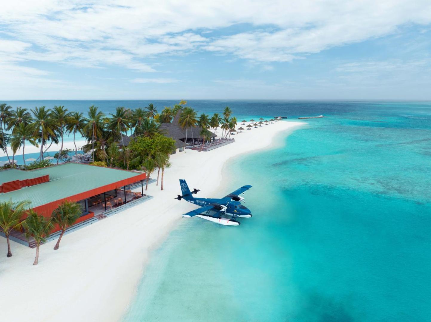 Hidroplāns pie Veligandu Maldives Resort Island krasta — kūrorta ēkas, palmas un balto smilšu pludmale saulainā dienā