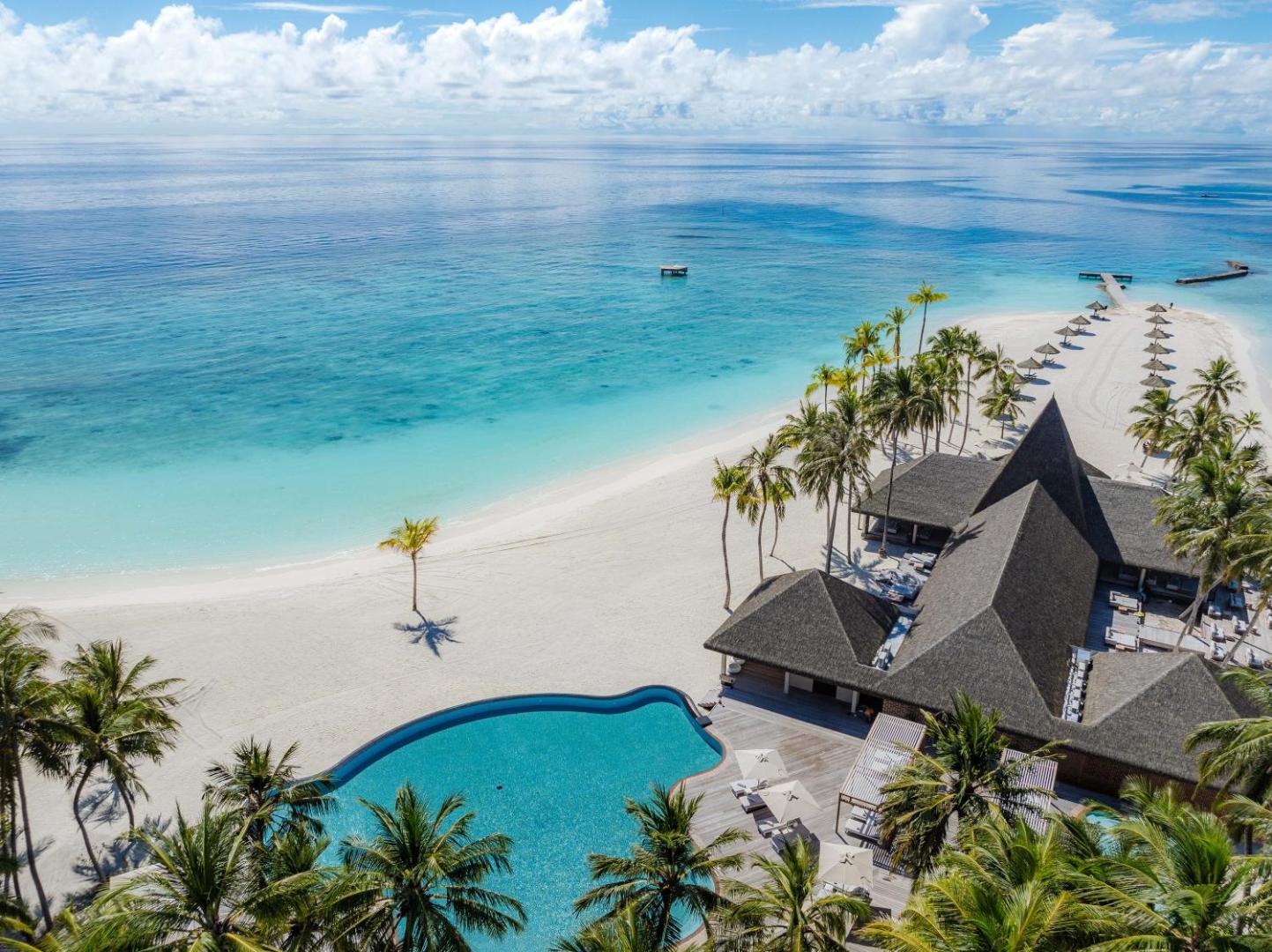 Veligandu Maldives Resort Island galvenais baseins pie pludmales ar palmām un skatu uz okeānu — atpūtas zona ar saulessargiem