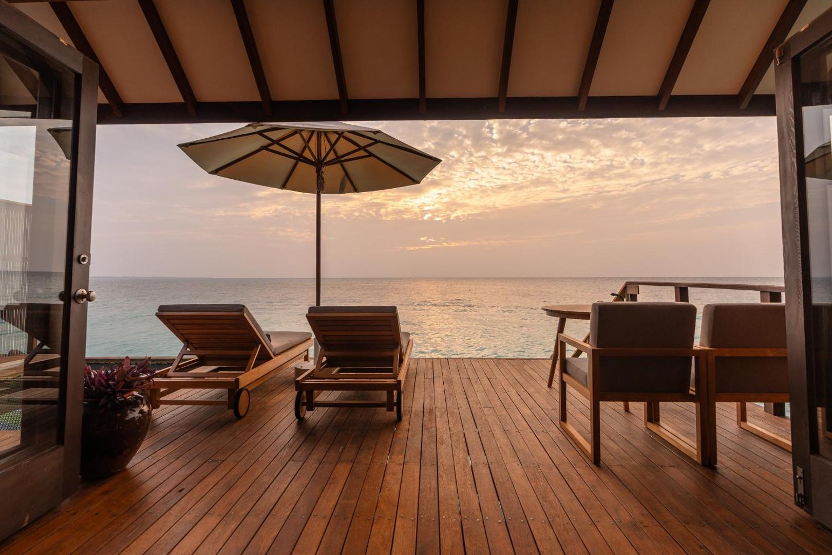 Veligandu Maldives Resort Island koka terase ar sauļošanās krēsliem un saulessargu tieši virs tirkīzzilā okeāna ūdens