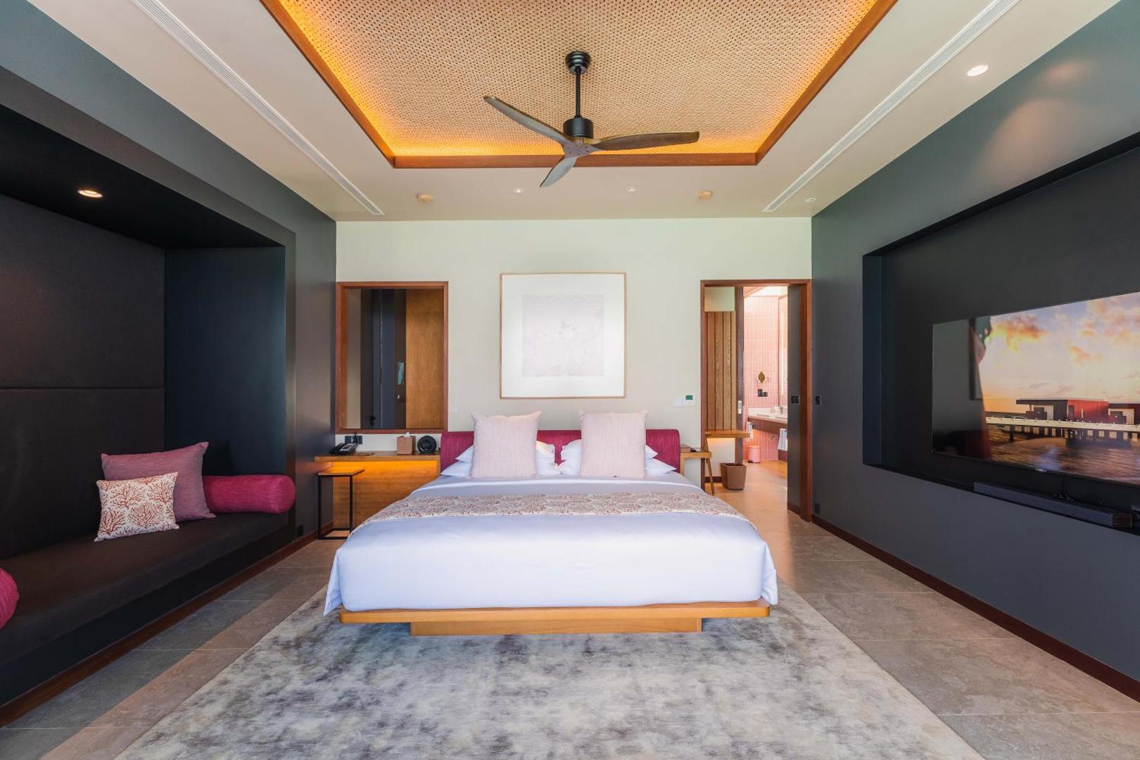 Veligandu Maldives Resort Island moderns viesnīcas numurs ar plašu gultu, atpūtas zonu un skatu uz okeānu ekrānā