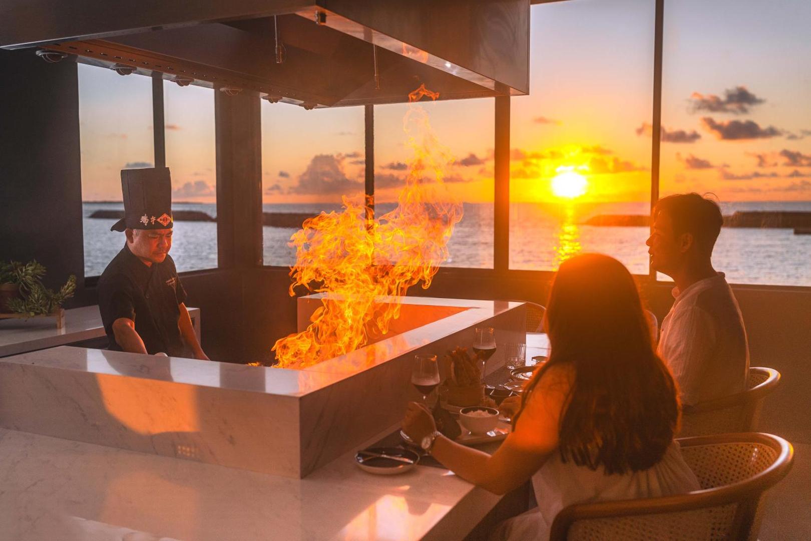 Veligandu Maldives Resort Island restorāna šefpavārs gatavo ēdienu uz atklātas uguns viesu priekšā saulrieta fonā pie okeāna