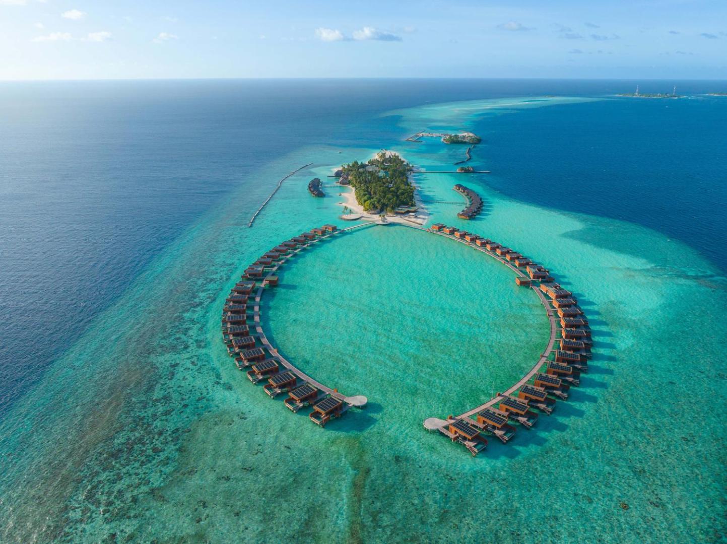 Veligandu Maldives Resort Island ūdens bungalo izvietojums puslokā virs dzidra tirkīza ūdens — skats no augšas uz koka laipām
