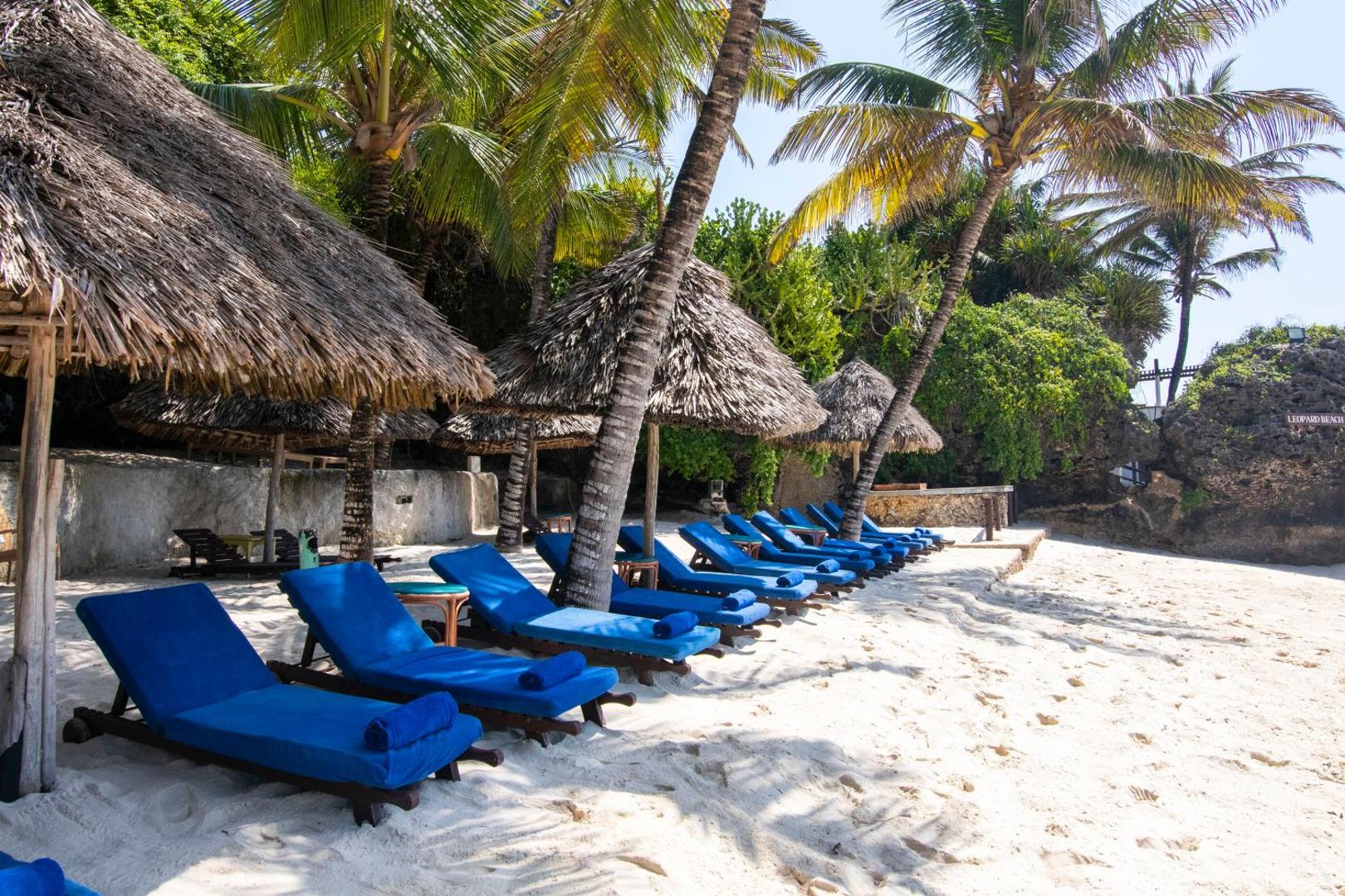 Leopard Beach Resort & Spa atpūtas zona pludmalē ar ziliem sauļošanās krēsliem zem tradicionālajām salmu saulessargiem un palmām