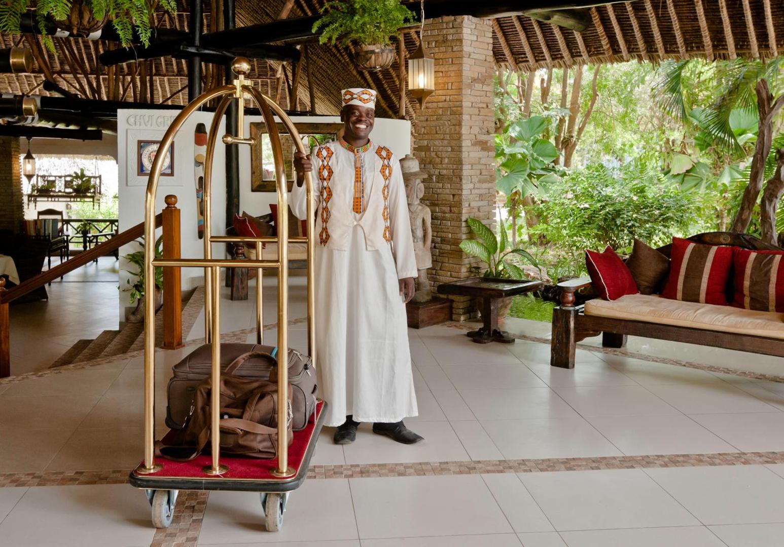 Leopard Beach Resort & Spa viesnīcas darbinieks tradicionālā tērpā sagaida viesus lobby zonā ar bagāžas ratiņiem