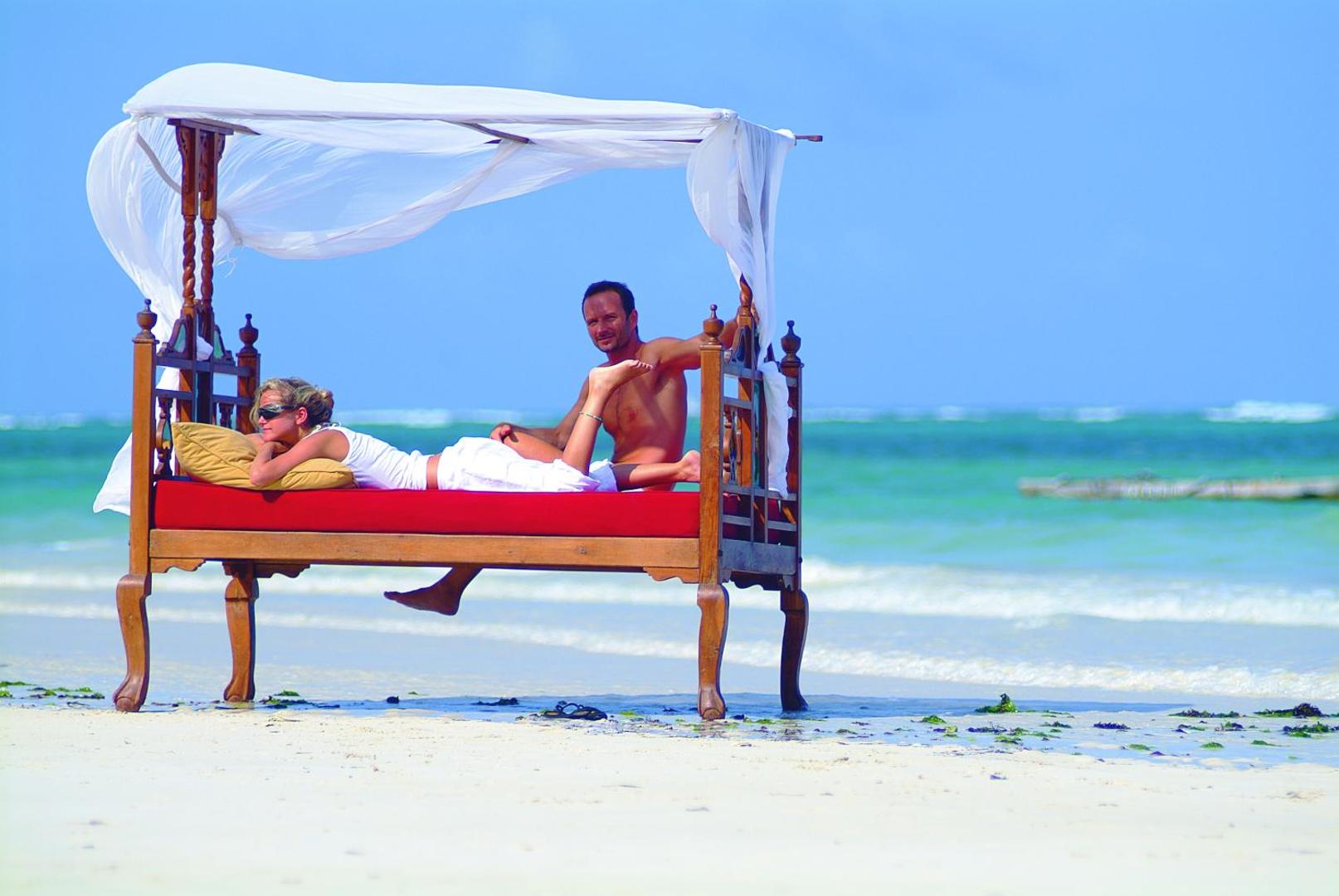 Pāris atpūšas uz greznas koka gultas ar baldahīnu Leopard Beach Resort & Spa pludmalē pie Indijas okeāna