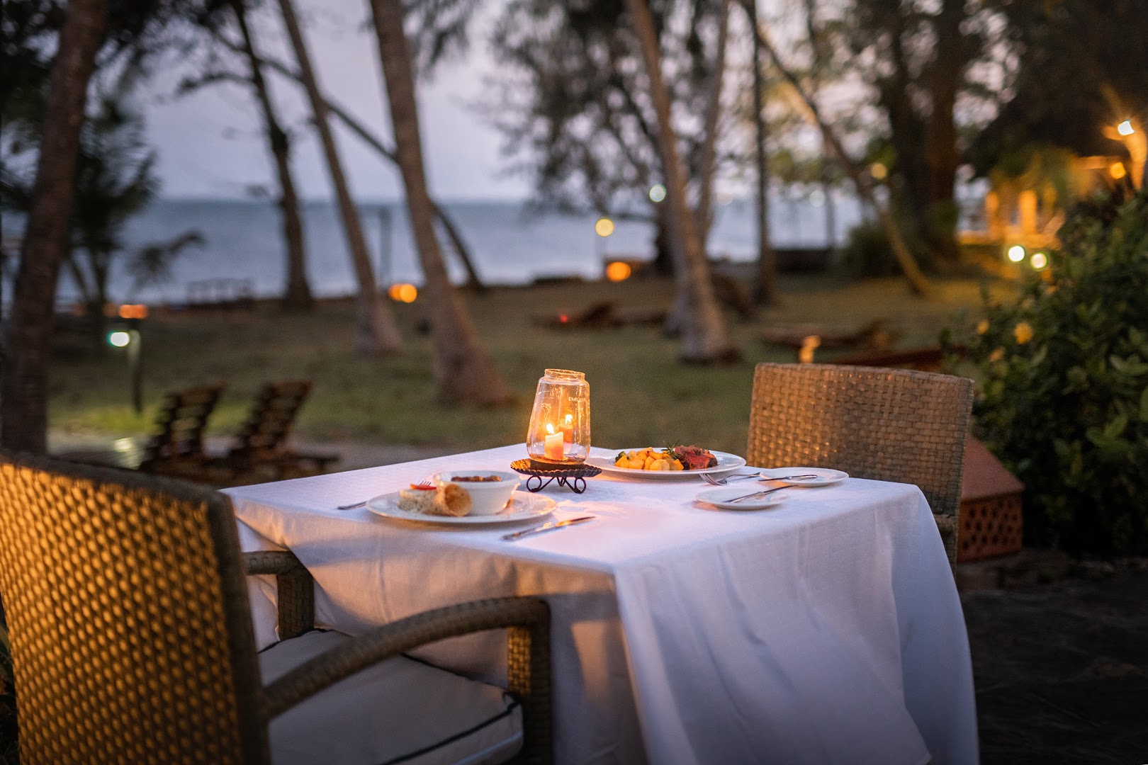Severin Sea Lodge eleganti klāts vakariņu galds ar svecēm un vietējiem ēdieniem viesnīcas dārzā krēslas stundā