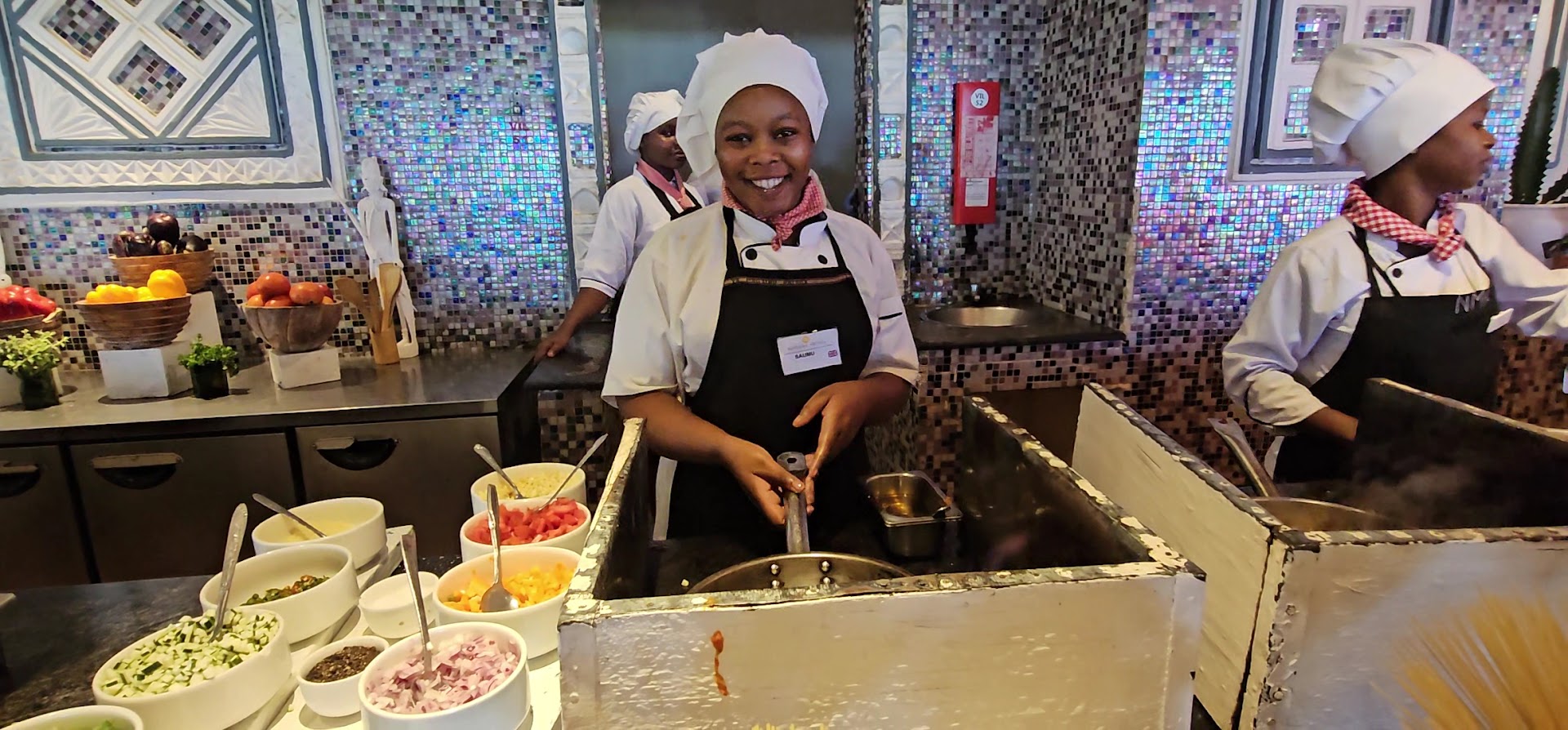Smaidīga pavāre gatavo ēdienu Neptune Village Beach Resort atvērtā tipa virtuvē Zanzibāras viesnīcas restorānā.