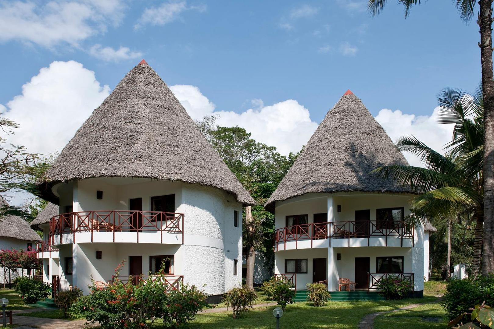 Neptune Village Beach Resort divstāvu bungalo ar tradicionāliem makuti niedru jumtiem un balkoniem tropu dārzā Zanzibāras piekrastē