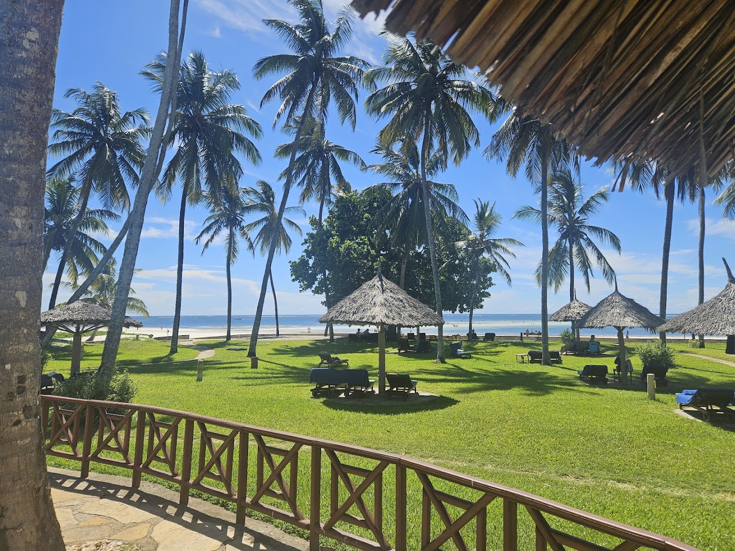 Skats no Neptune Village Beach Resort terases uz Indijas okeānu, palmām un atpūtas zonu ar saulessargiem zālienā