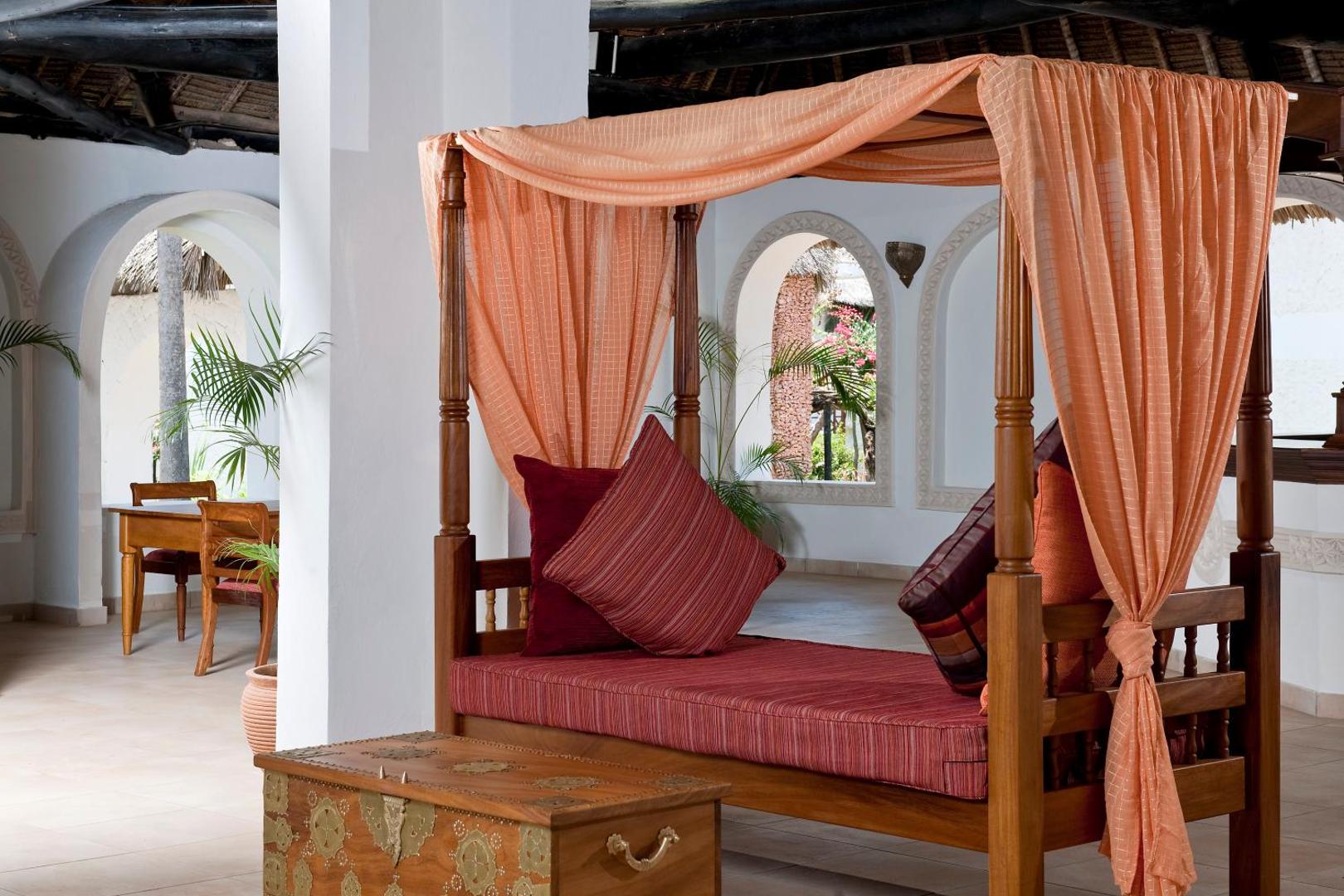 Tradicionāla koka gulta ar baldahīnu un dekoratīviem spilveniem Neptune Village Beach Resort atpūtas zonā Zanzibārā.