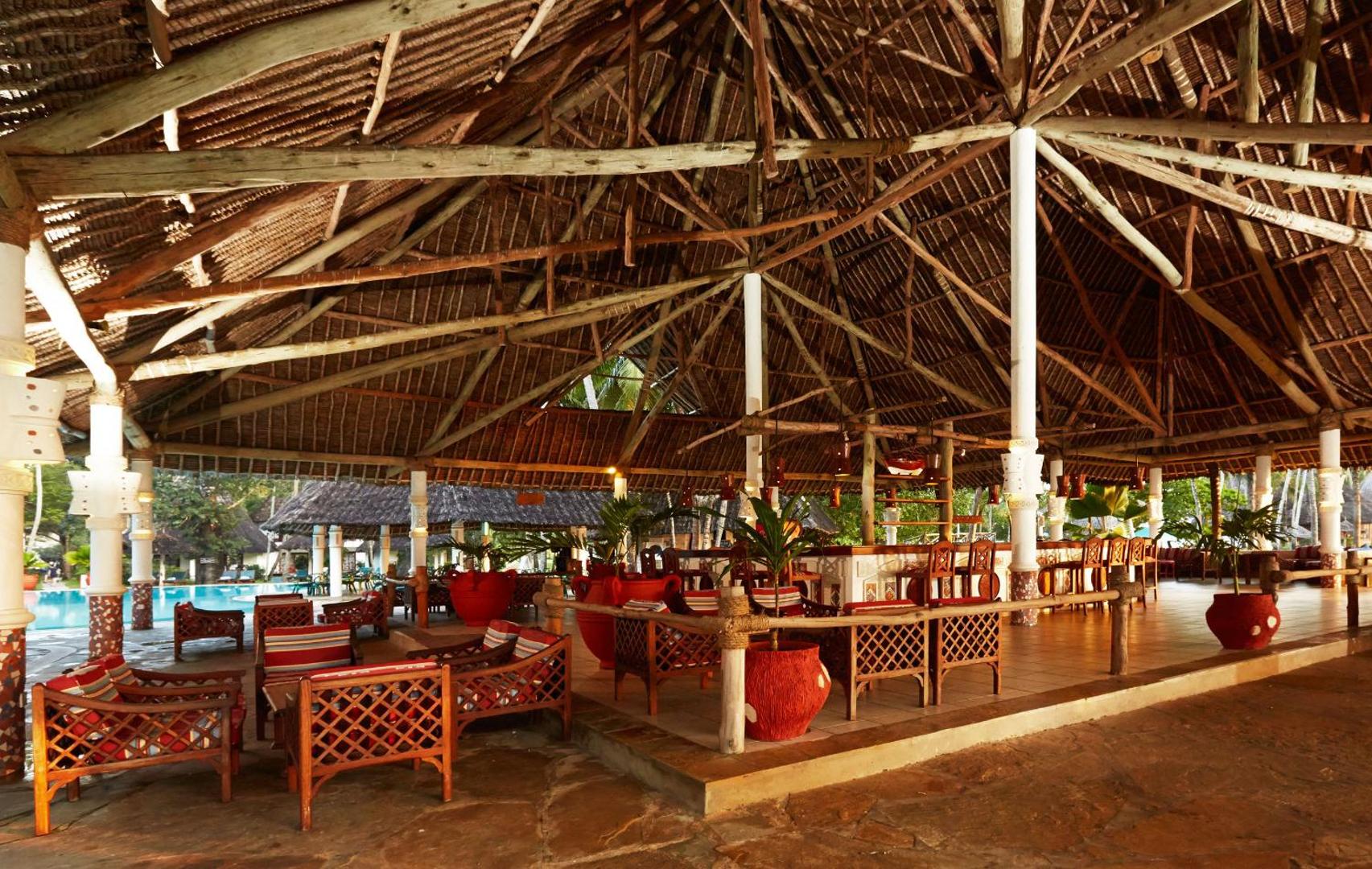 Neptune Village Beach Resort plašais bārs zem tradicionālā makuti jumta Zanzibārā — atpūtas krēsli un skats uz baseinu