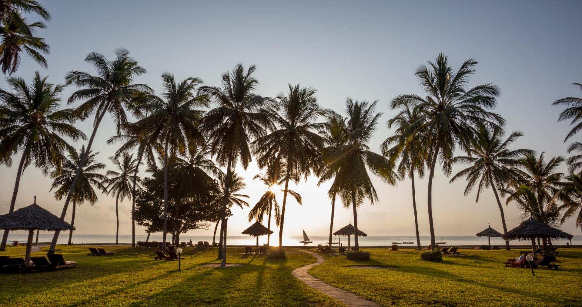 Neptune Village Beach Resort dārzs saulrietā ar palmām, atpūtas krēsliem un skatu uz okeānu Zanzibāras piekrastē