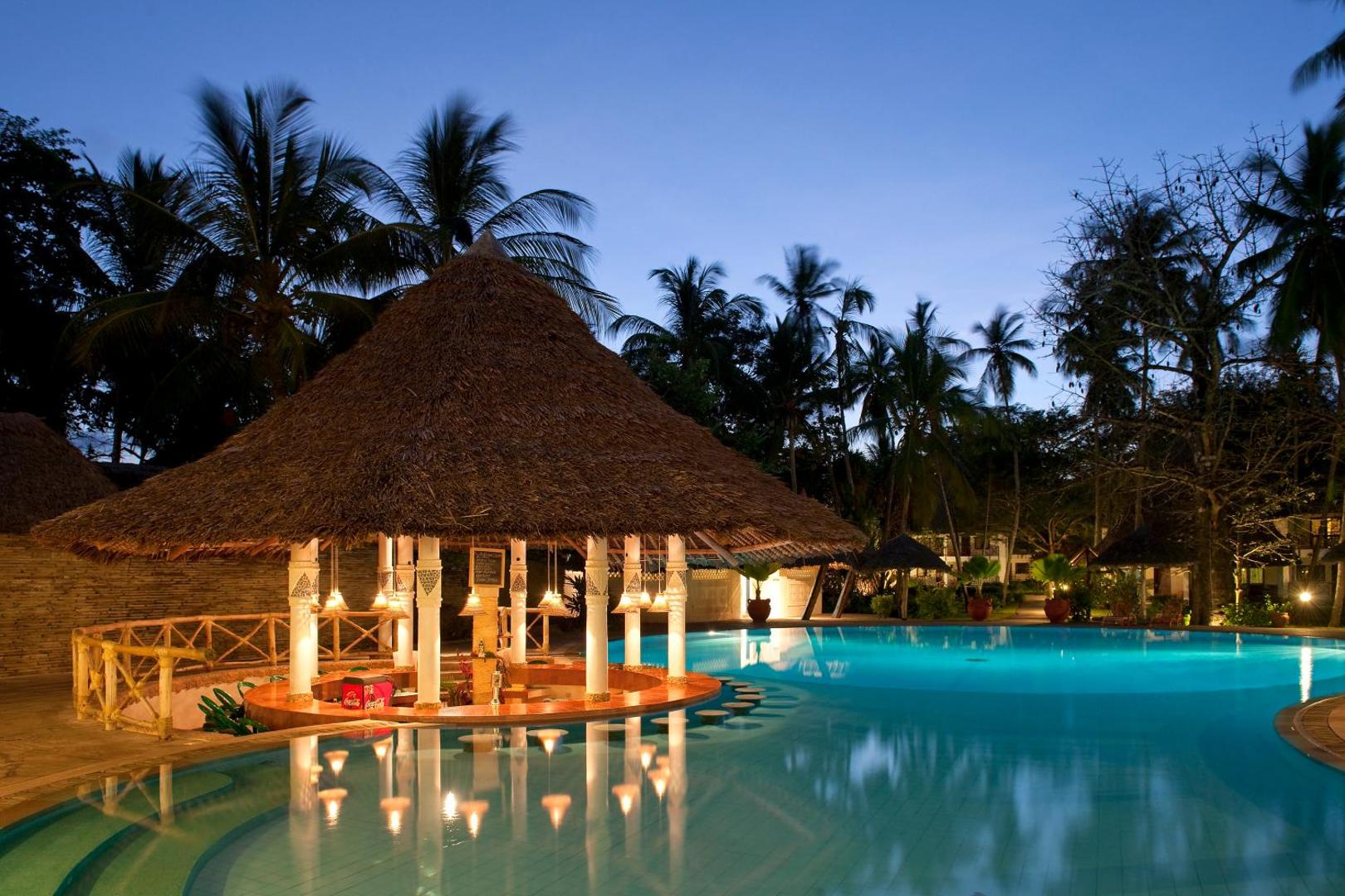 Neptune Village Beach Resort baseina bārs vakarā ar salmu jumtu un siltu apgaismojumu Zanzibāras kūrortā