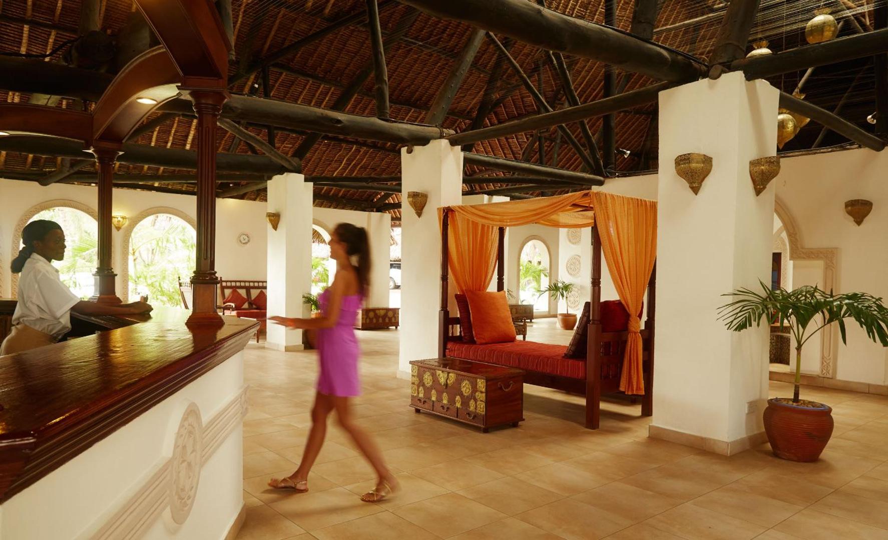 Neptune Village Beach Resort reģistratūra ar koka apdari un tradicionālu jumtu Zanzibārā — viesu uzņemšanas zona ar atpūtas dīvānu