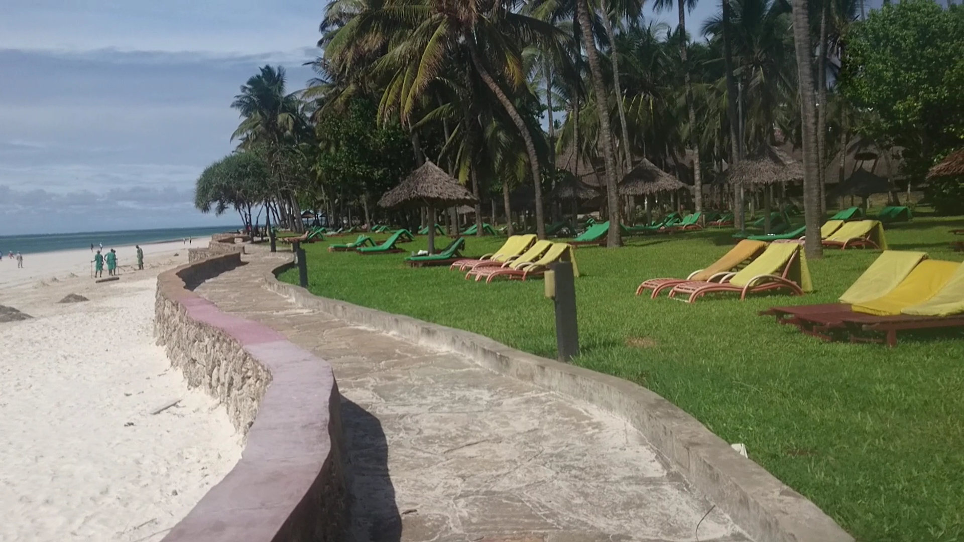 Neptune Village Beach Resort atpūtas zona zālienā ar krāsainiem sauļošanās krēsliem un saulessargiem pie pludmales