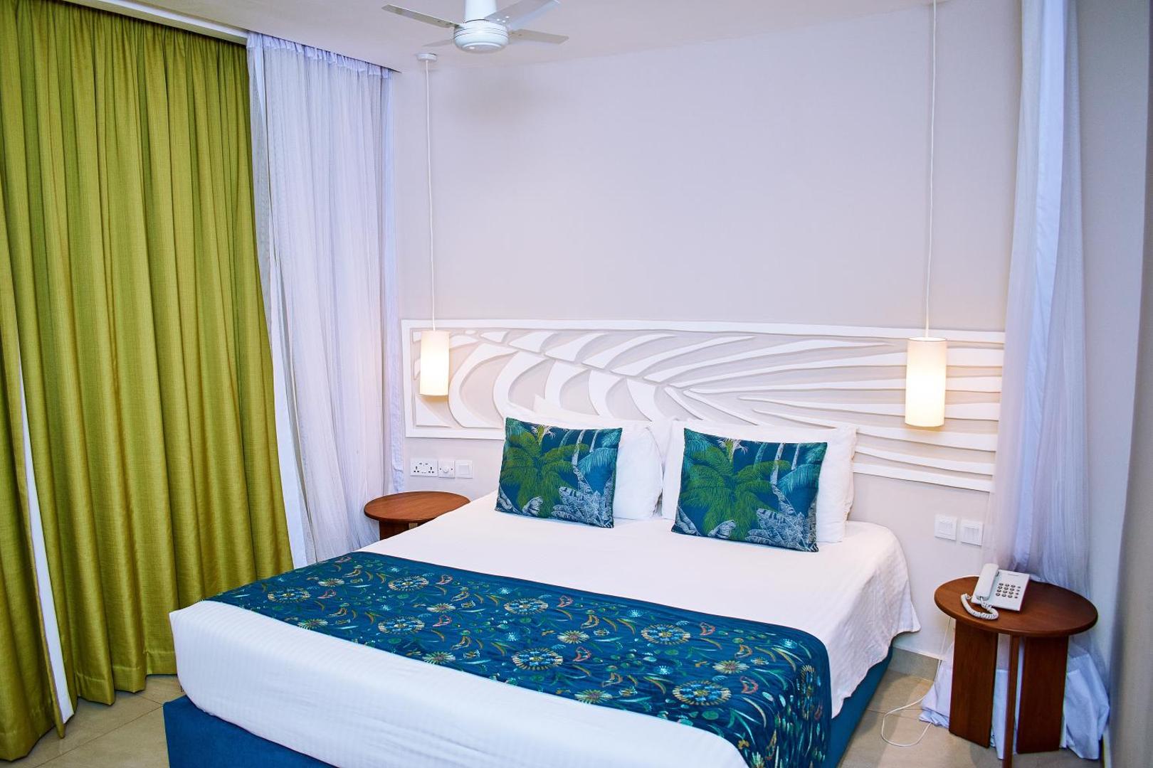 Moderns Neptune Village Beach Resort numurs ar ziliem akcentiem, rakstainu gultas pārklāju un dekoratīvu sienas paneli