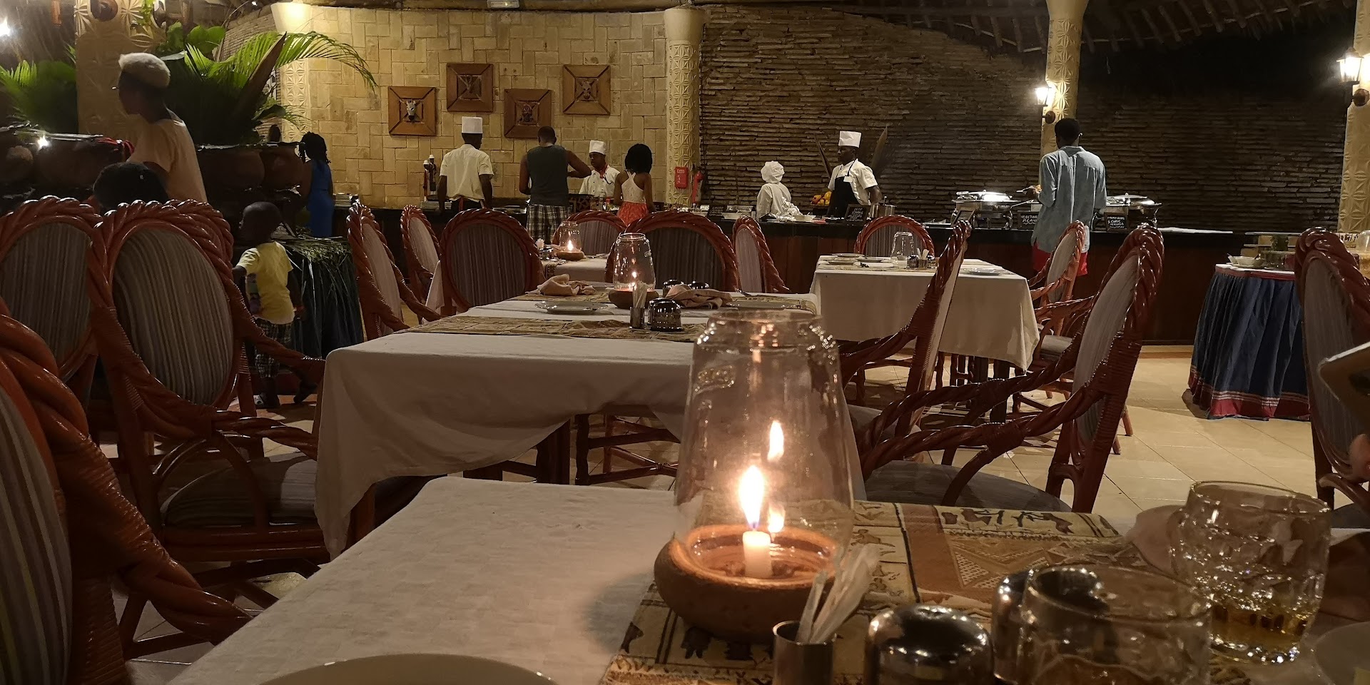 Vakariņas Neptune Village Beach Resort restorānā ar svecēm uz galdiem un bufetes zonu fonā Zanzibāras kūrortā.
