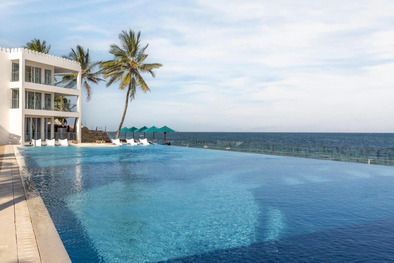 Bamburi Beach Hotel modernais baseins pie okeāna ar baltiem atpūtas krēsliem un zaļiem saulessargiem