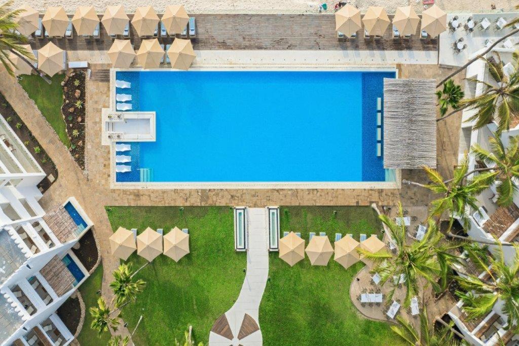 Bamburi Beach Hotel āra baseins no putna lidojuma Kenijas piekrastē — zils taisnstūra baseins, sauļošanās krēsli ar saulessargiem un palmas