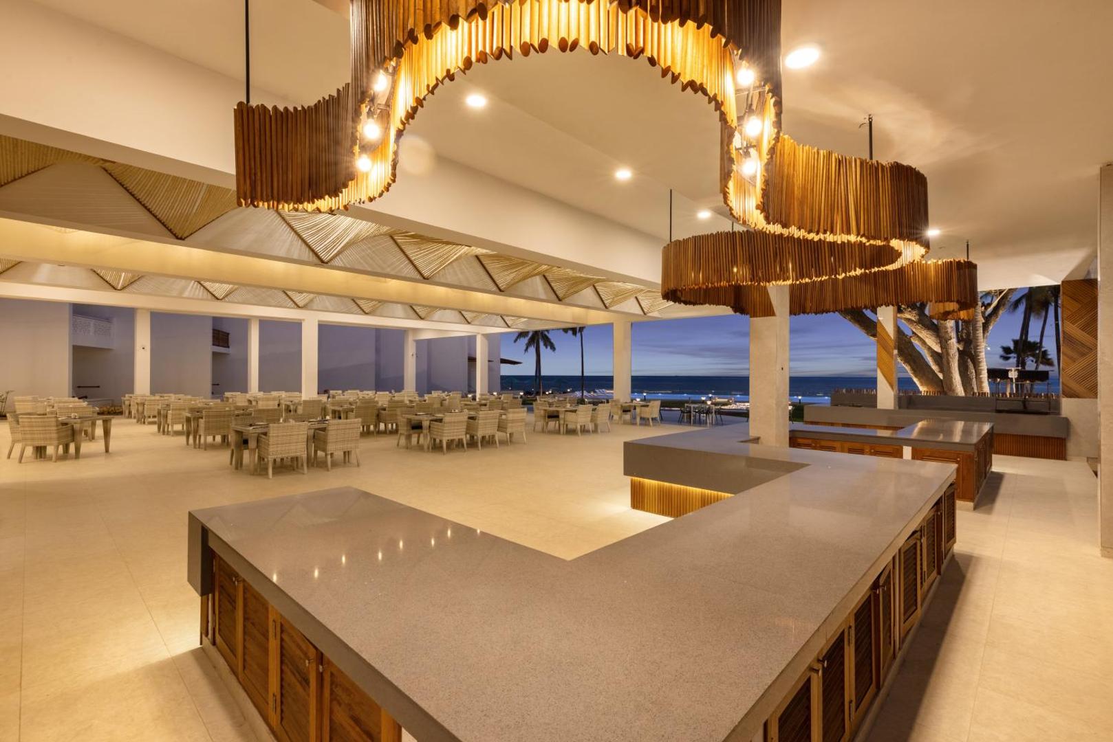 Bamburi Beach Hotel plašais bārs un restorāna zona ar unikālu koka dizaina lustru un skatu uz vakara debesīm.